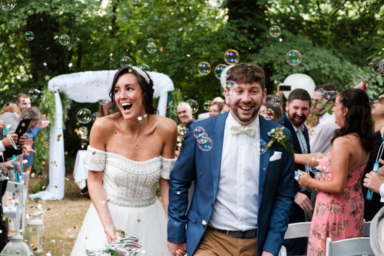bride and groom walk down the aisle at outdoor ceremony with bubbles